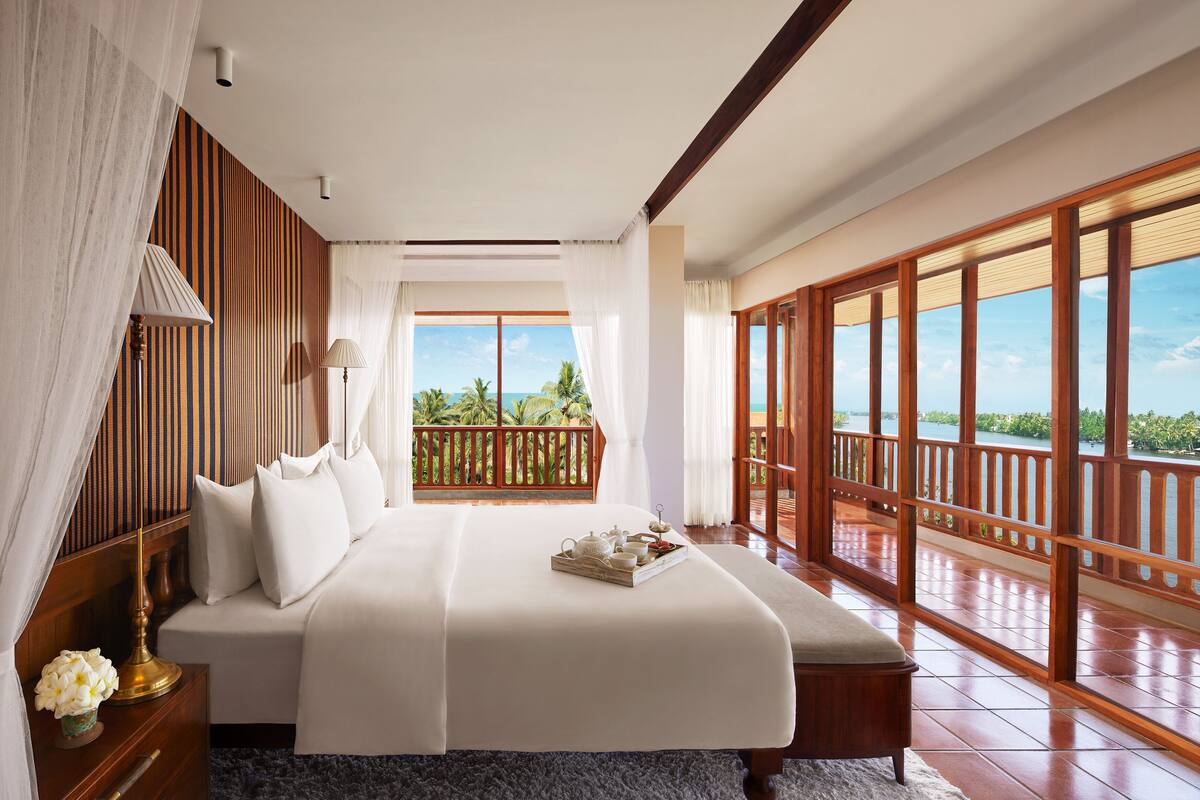 Un dormitorio amplio con una cama grande, cabecera de madera y vistas al océano a través de ventanas amplias.
