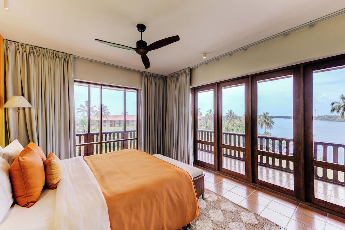 Habitación de hotel con una cama grande, ventilador de techo y balcón con vista al mar.