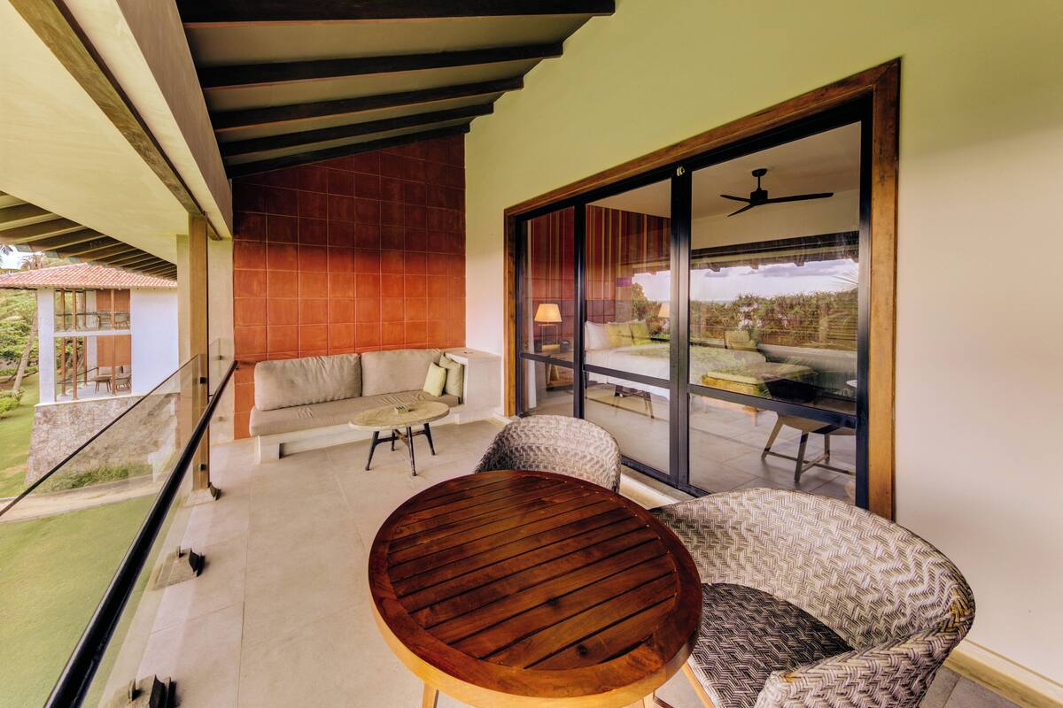 Un balcón con una mesa de madera, un sillón estampado y un sofá con cojines.