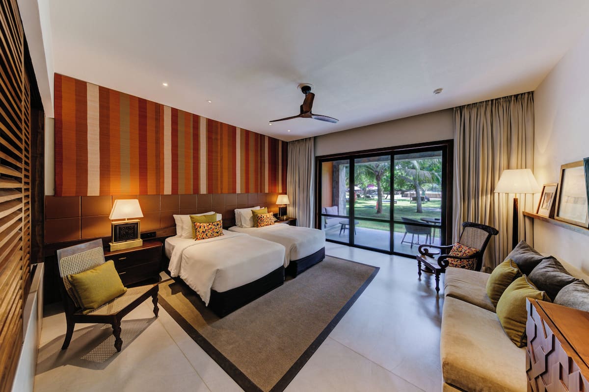 Habitación de hotel con dos camas, un sofá, una silla, un escritorio y un ventanal con vistas al exterior.