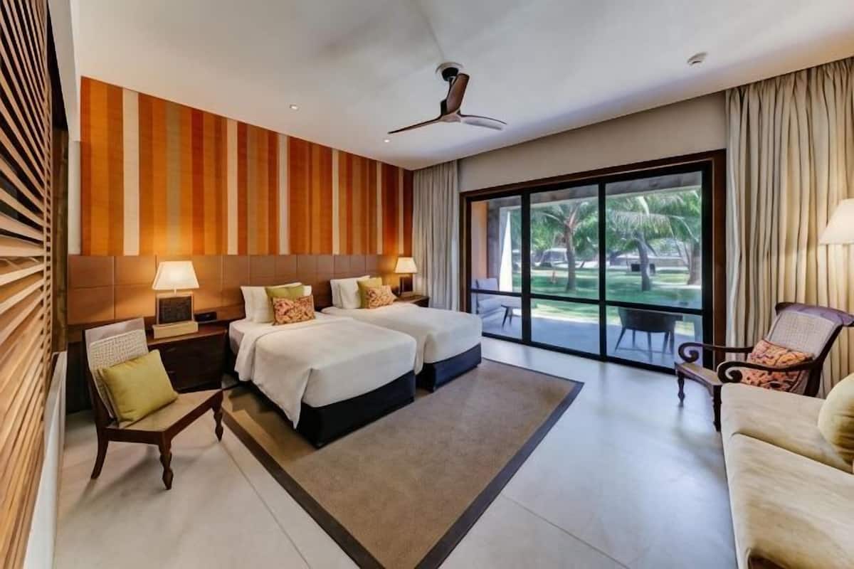 Habitación de hotel con dos camas, una zona de estar con un sillón, un ventanal con vistas y un ventilador de techo.