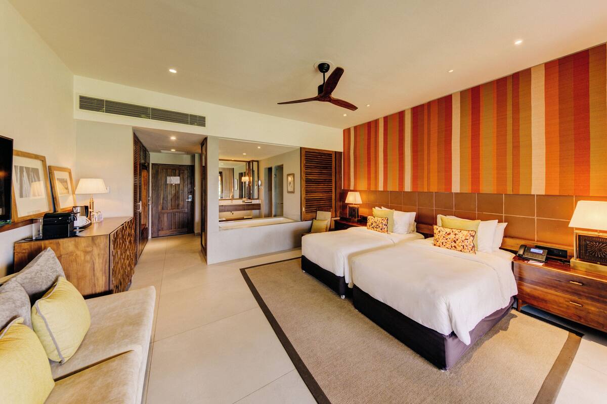 Habitación de hotel con dos camas, un sofá, un escritorio y un espejo grande.