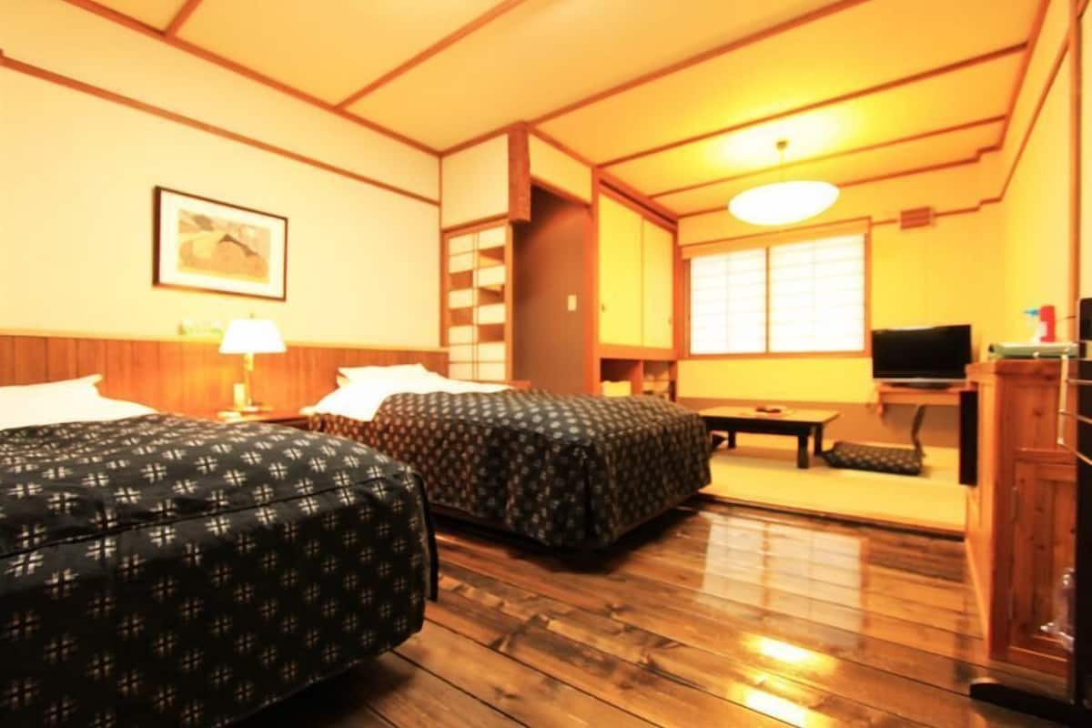 A hotel room with two beds, a desk, a television, and a window.