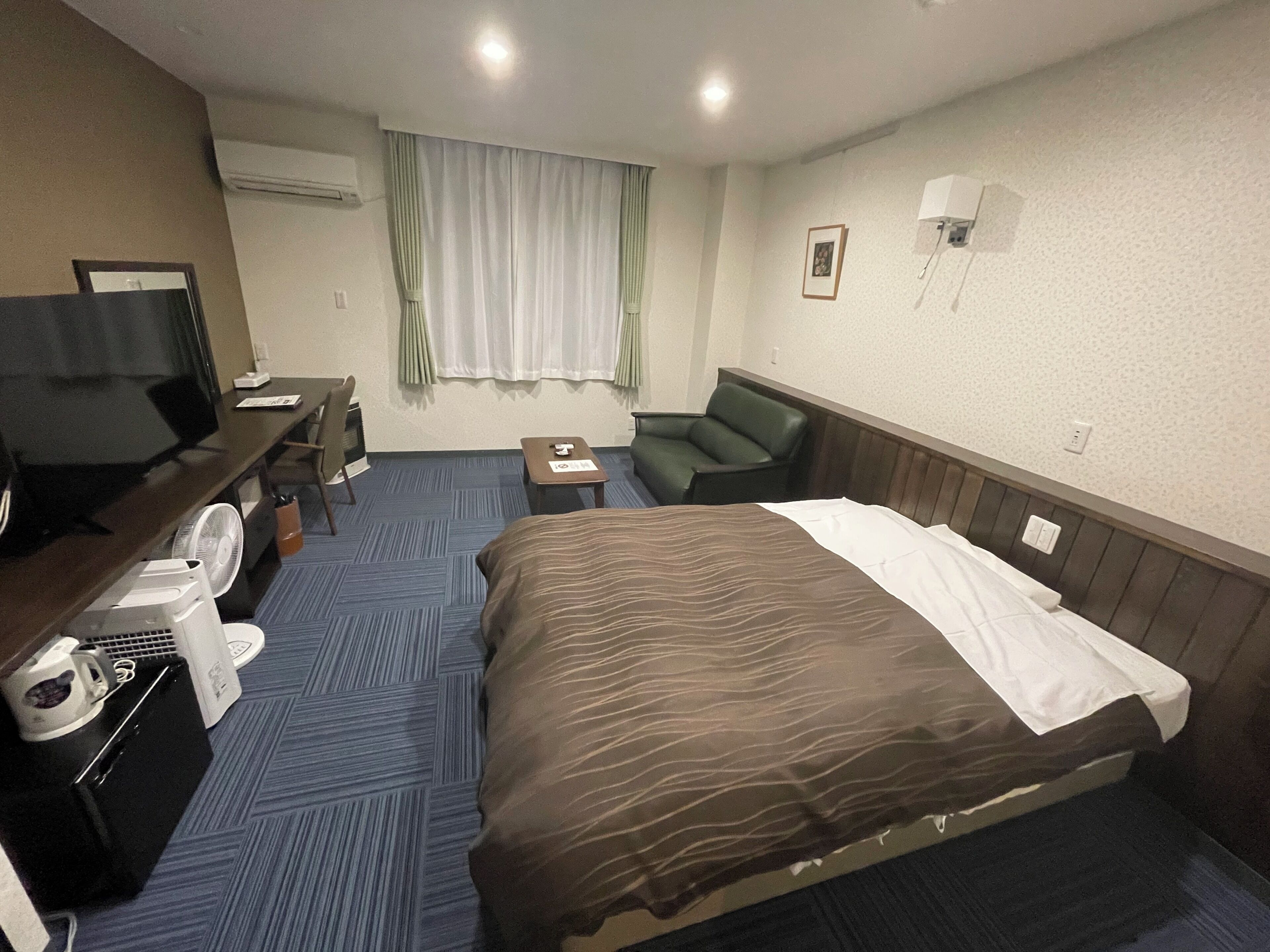 A hotel room with a bed, a desk with a computer, a chair, a TV, and a coffee maker.