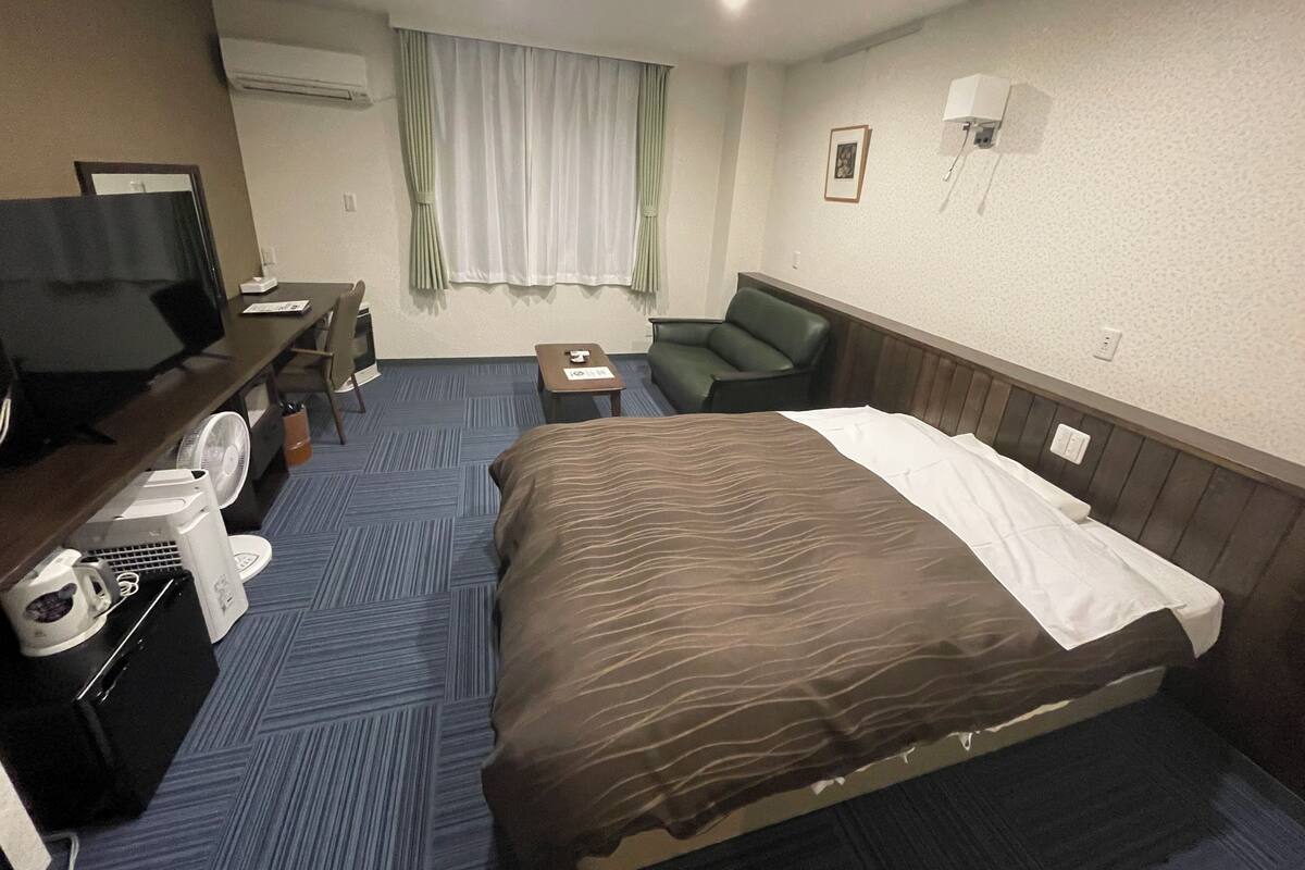 A hotel room with a bed, a desk with a computer, a chair, a TV, and a coffee maker.