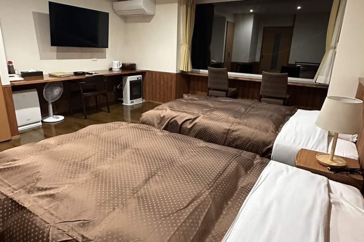 A hotel room with two beds, a desk, a chair, a TV, and a mirror.