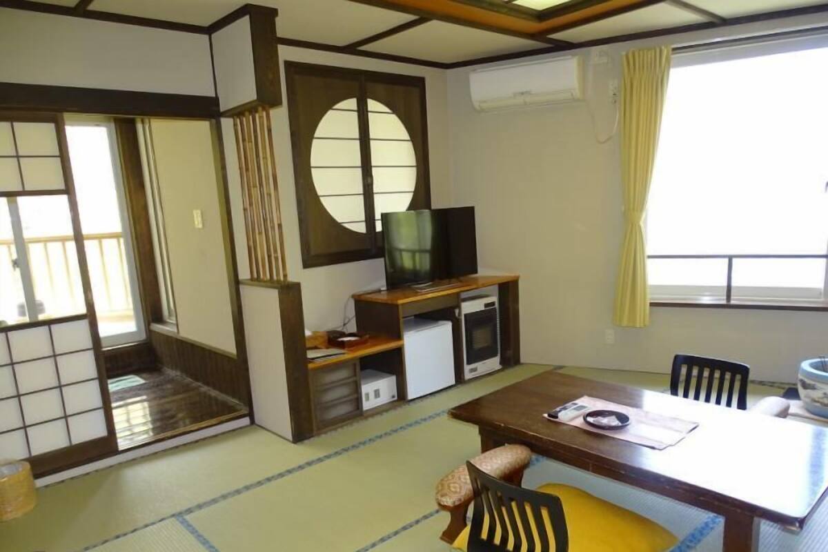 A traditional Japanese room with tatami flooring, a low table, a television, and a sliding door.