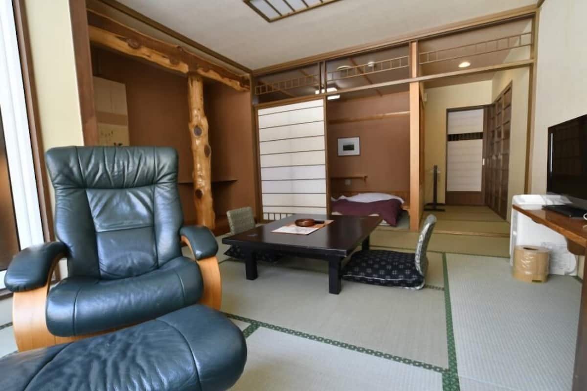 A traditional Japanese room with tatami flooring, a black leather chair, a low table, and sliding doors.