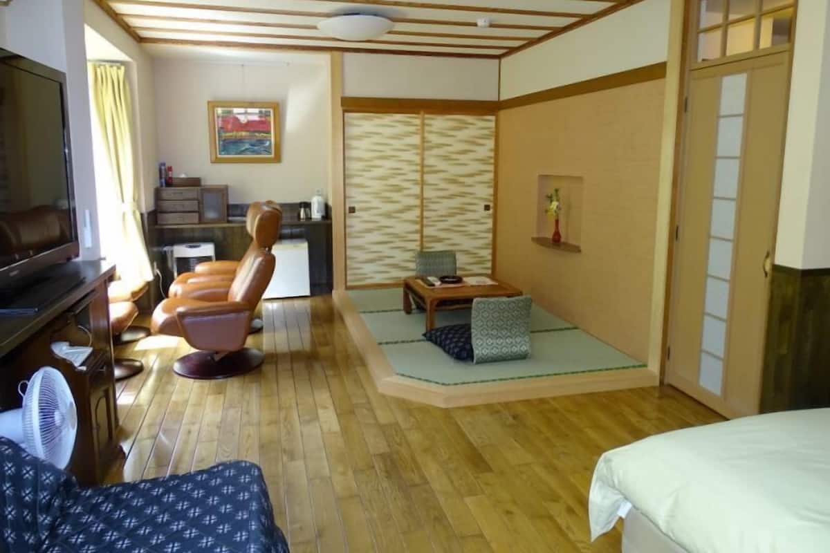 A traditional Japanese-style room with tatami flooring, a low table, a sofa, a television, and a sliding door.