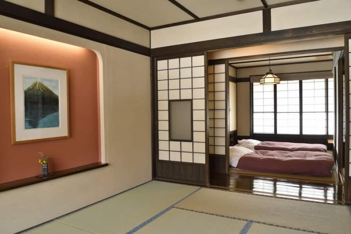 A traditional Japanese room with tatami flooring, a bed with pink bedding, a framed picture on the wall, and a sliding door with a grid pattern.