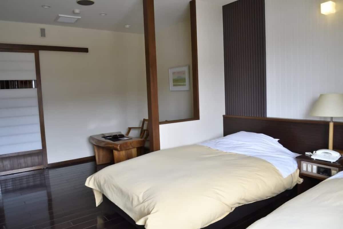 A hotel room with a bed, bedside table, lamp, and a small desk with a chair.