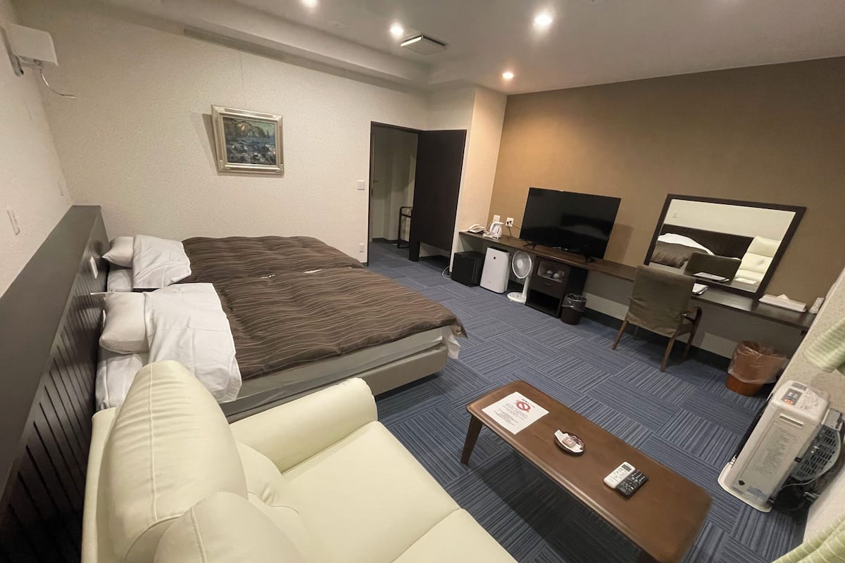 A hotel room with a bed, a sofa, a desk with a computer, a TV, and a small table with a remote control.