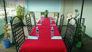 A conference room with a long table covered in a red tablecloth, surrounded by chairs, and potted plants. - Cingaki Hotel (Mombasa)