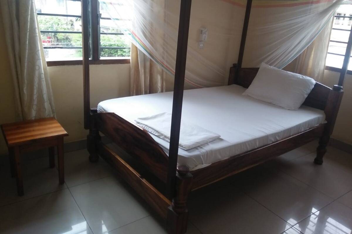 A single bed with a canopy, a small wooden table, and a window with curtains.