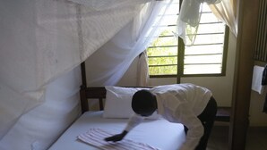 A bed with a mosquito net, a white pillow, and a person bending over the bed. - Cingaki Hotel (Mombasa)