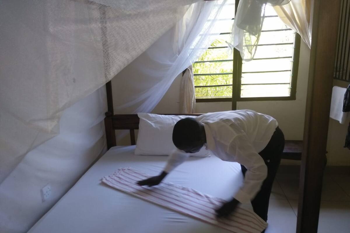 A bed with a mosquito net, a white pillow, and a person bending over the bed.