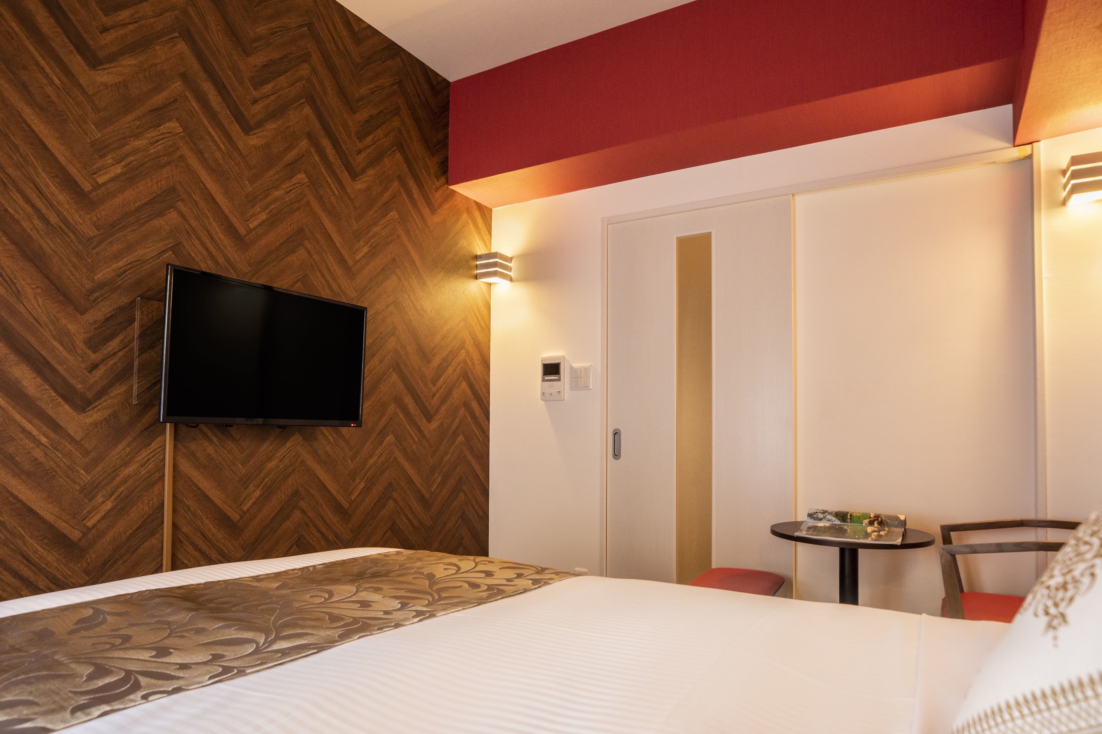 A hotel room with a large bed, a television mounted on the wall, a small table with a chair, and a wardrobe with sliding doors.