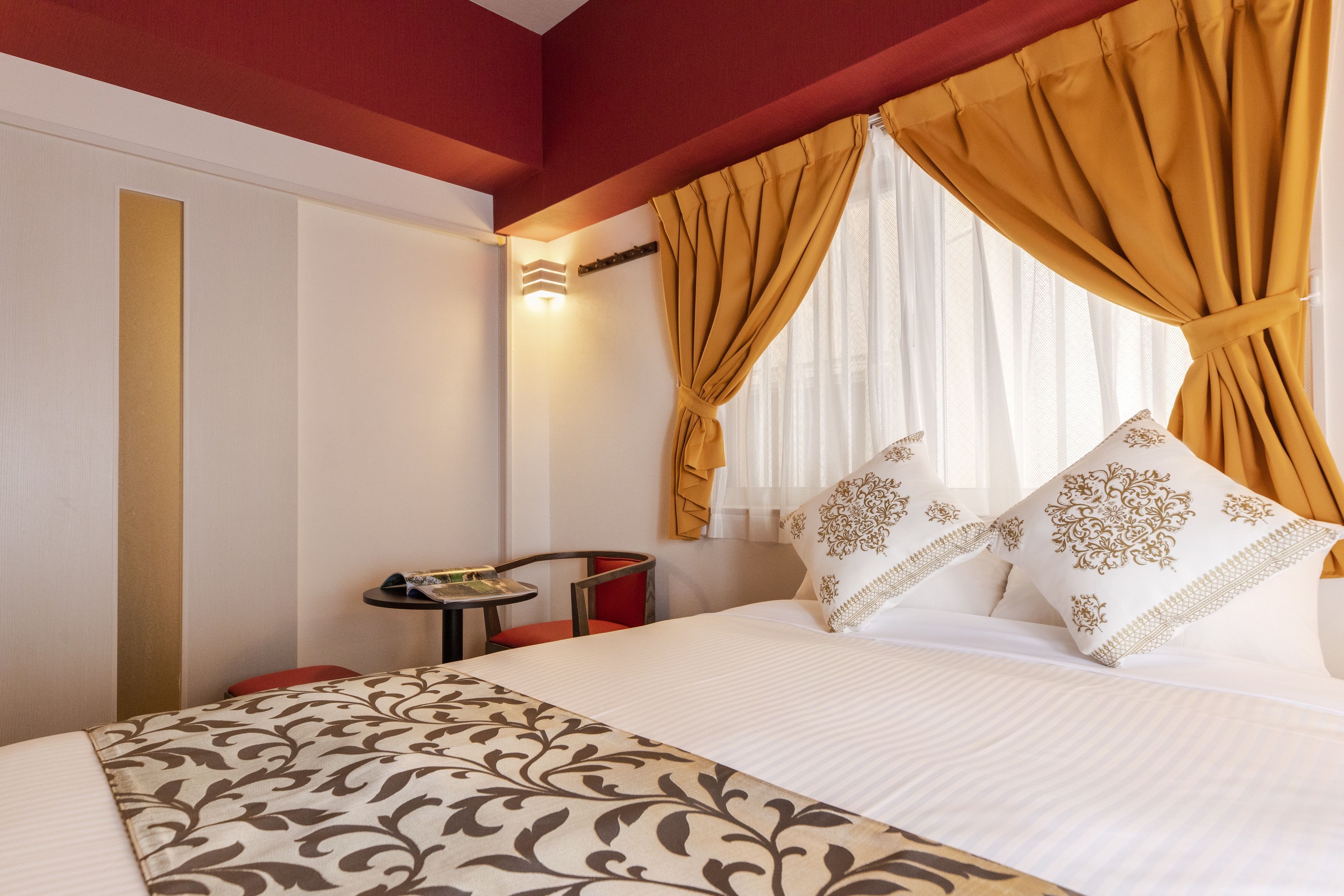 Habitación de hotel con cama, una mesita, una silla y ventana con cortinas.