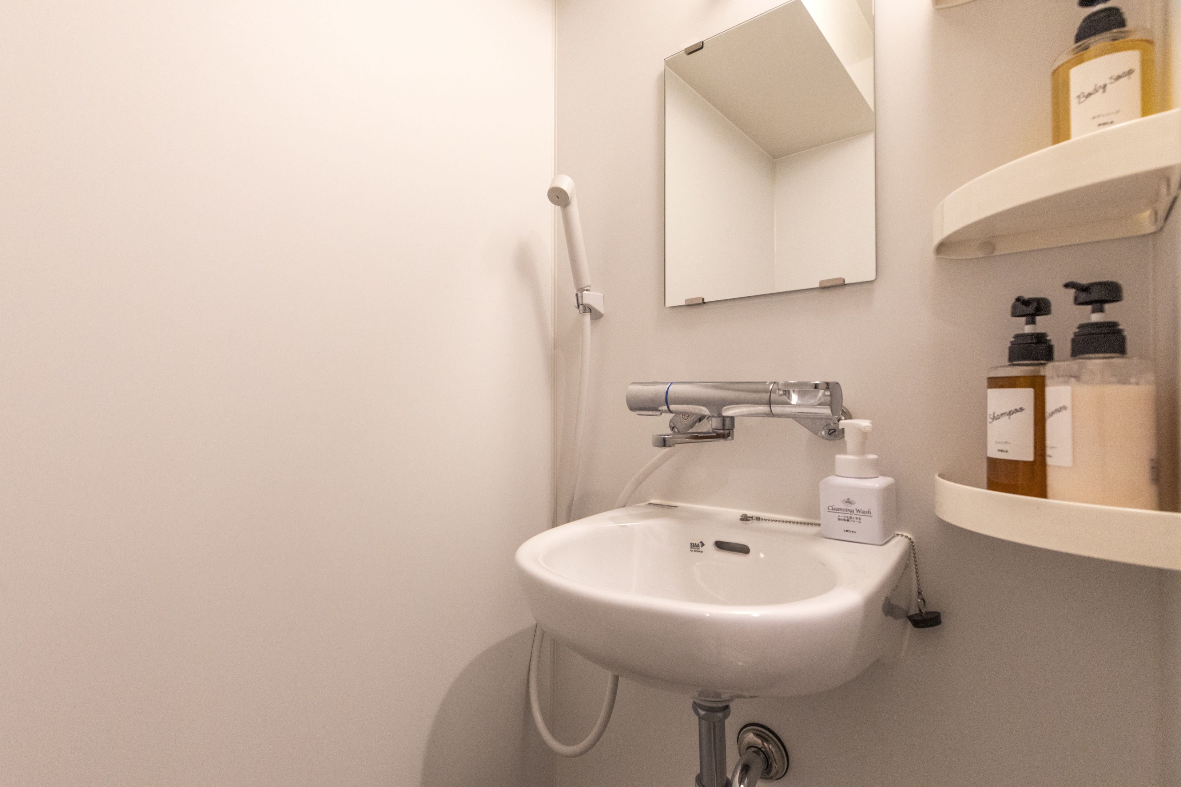 Un baño con un lavamanos blanco, un espejo y un estante con artículos de aseo.