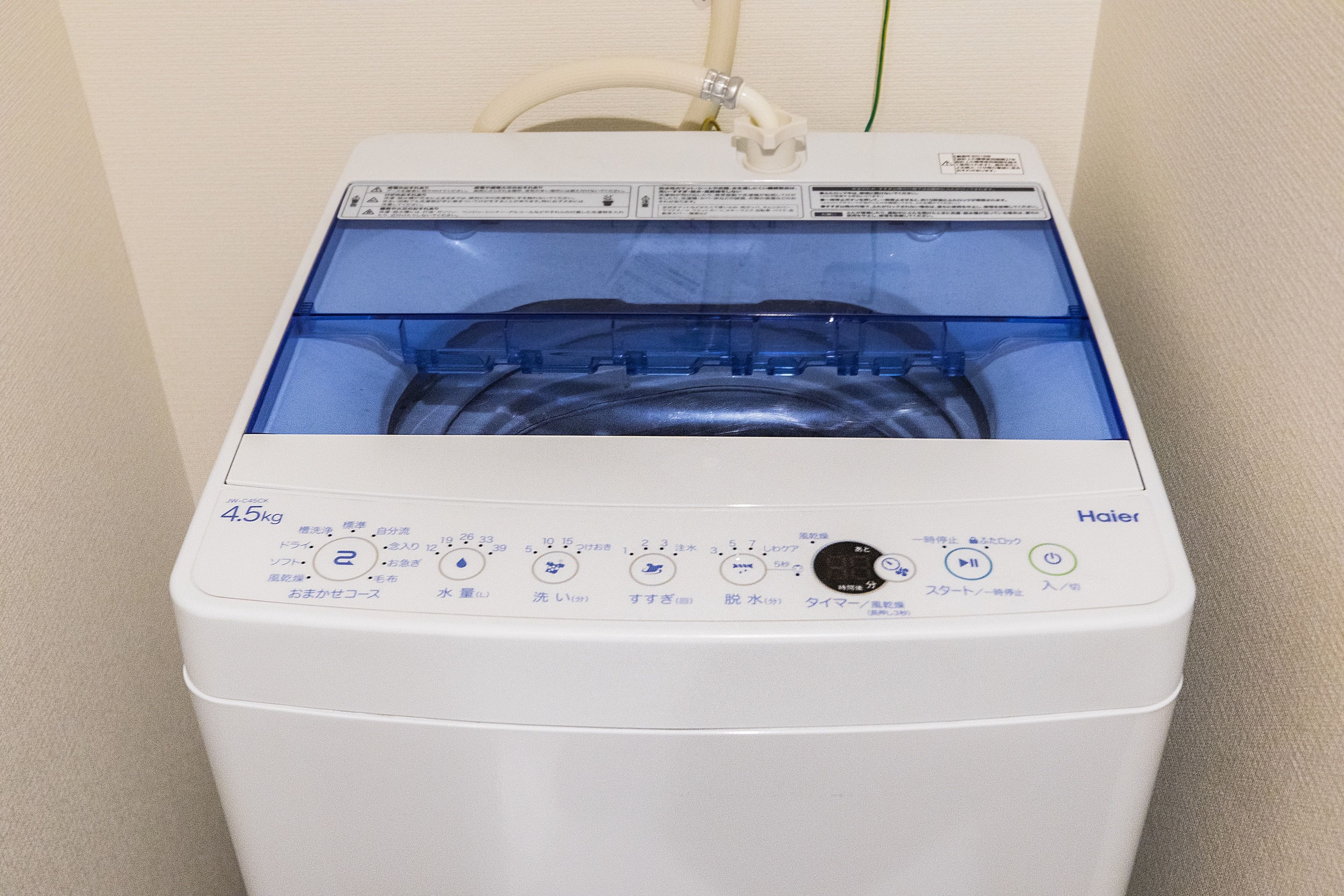 A white Haier washing machine with a transparent drum, control panel with Japanese instructions, and a water inlet hose.