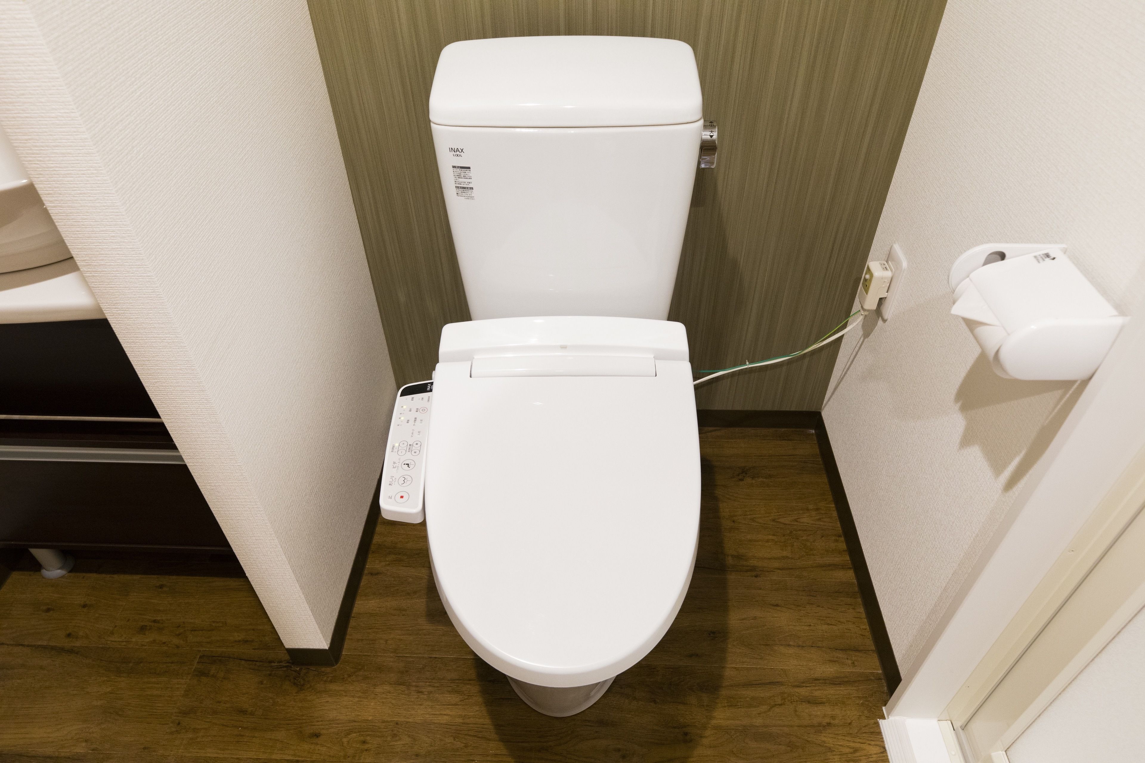 A modern bathroom with a white toilet, a wall-mounted paper towel dispenser, and a visible electrical outlet.