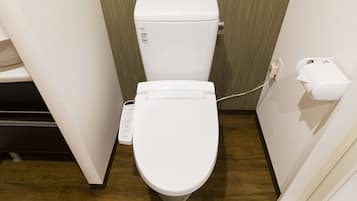 A modern bathroom with a white toilet, a wall-mounted paper towel dispenser, and a visible electrical outlet.