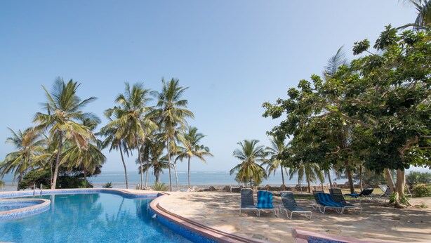 A pool area with lounge chairs and palm trees, overlooking a beach. - Cho ka Cottages (Mombasa)