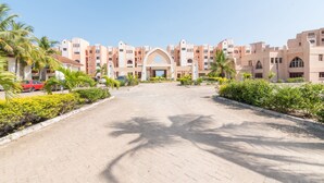 A paved pathway leading to a building with a central archway, surrounded by palm trees and greenery. - Cho ka Cottages (Mombasa)