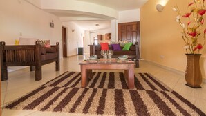 A living room with a wooden sofa, a coffee table set with dinnerware, and a striped rug. - Cho ka Cottages (Mombasa)