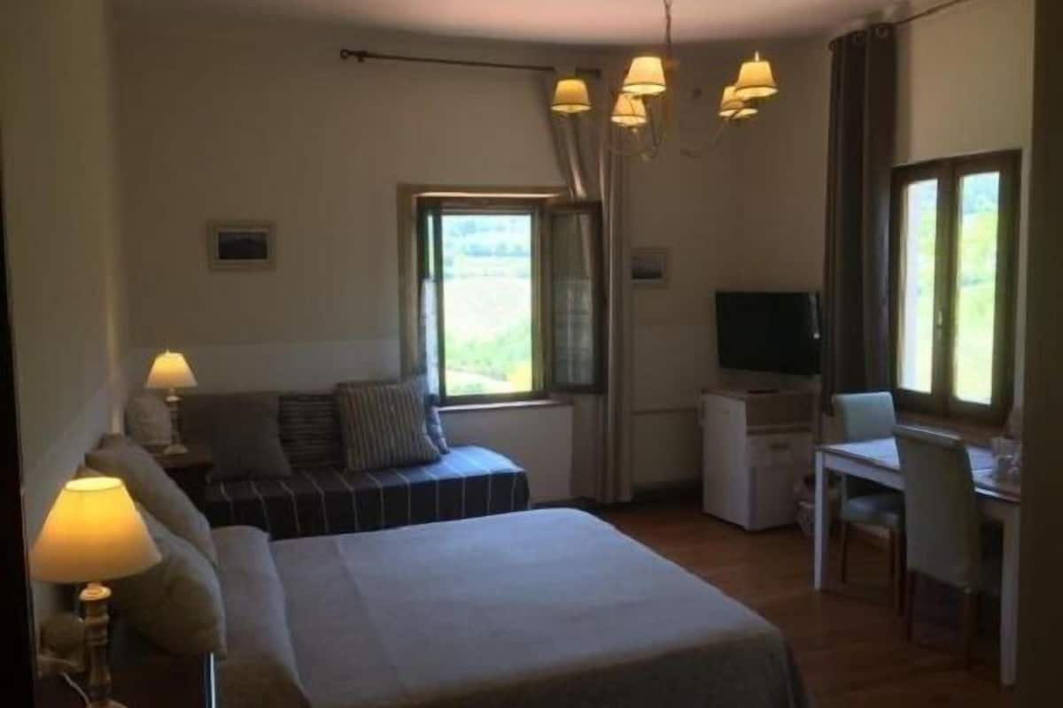 A bedroom with a bed, bedside lamps, a desk, a chair, a television, and a window with curtains.