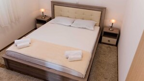 A neatly made bed with a wooden headboard, two bedside tables with lamps, and a carpeted floor. - Apartman Kuzmanic Kastela (Kaštel Stari)