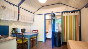 Une petite pièce comprenant une table en bois, des chaises, un lit, une poubelle et un rideau coloré à rayures.