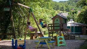 Un terrain de jeux avec des balançoires, une cabane et une table de pique-nique.
