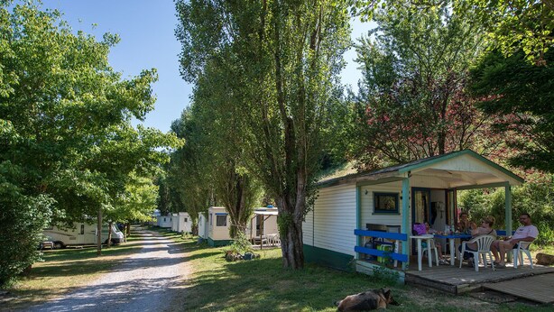 Un terrain de camping avec des mobil-homes, un espace de repos couvert et un chien allongé par terre.