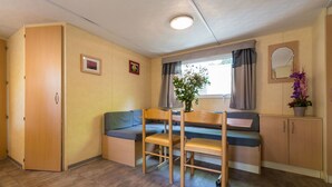 Une pièce de taille modeste, comprenant un bureau en bois, un banc bleu rembourré, une chaise en bois, un petit meuble et une fenêtre avec des rideaux.