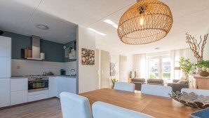 A modern kitchen with white cabinets, a wooden dining table, and a hanging light fixture. - Holiday home for 6 people in Wemeldinge (Wemeldinge)