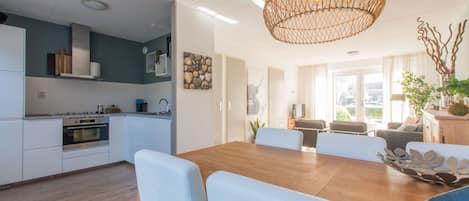 A modern kitchen with white cabinets, a wooden dining table, and a hanging light fixture.
