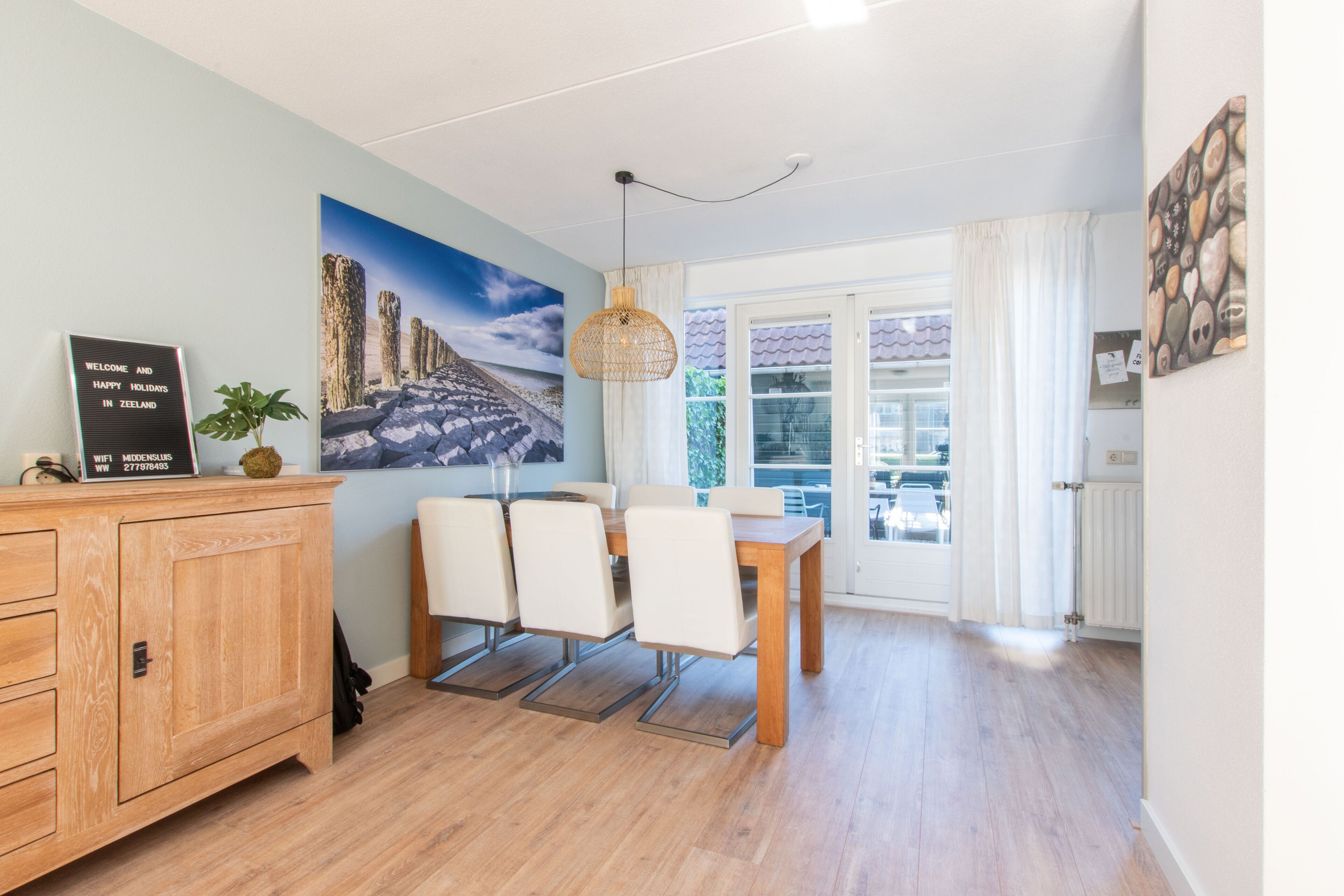 A dining area with a wooden table and chairs, a hanging light fixture, and a painting on the wall.