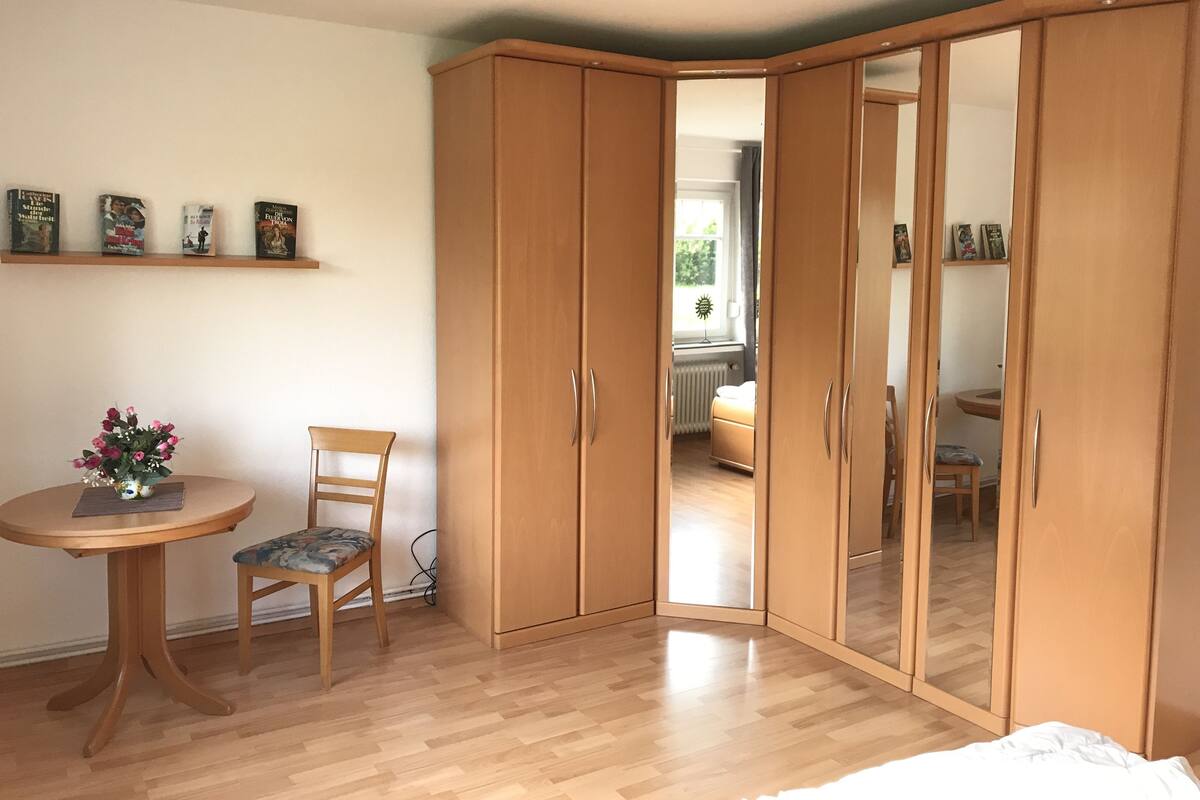 Makuuhuoneessa on puinen vaatekaappi, pyöreä pöytä ja tuoli sekä pieni kasvi.