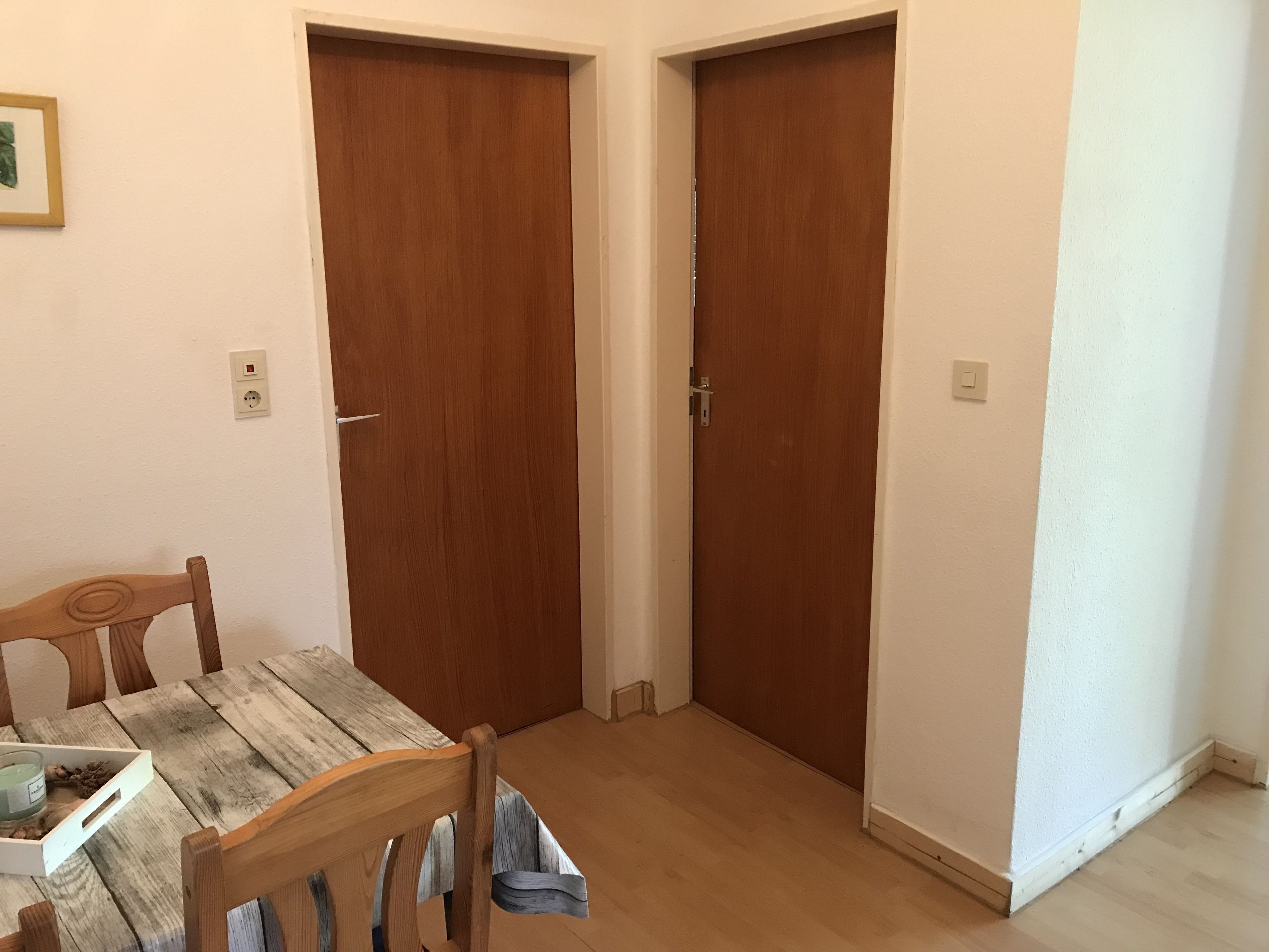 Ein Zimmer mit einem Holztisch, zwei Holztüren und einem Lichtschalter an der Wand.