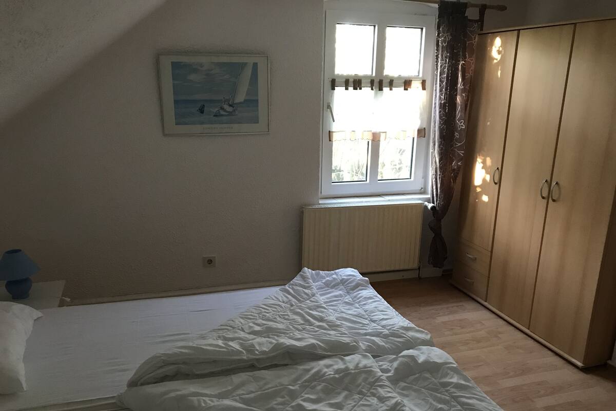 Makuuhuone, jossa on sänky, patteri, vaatekaappi ja ikkuna, jossa on verhot.