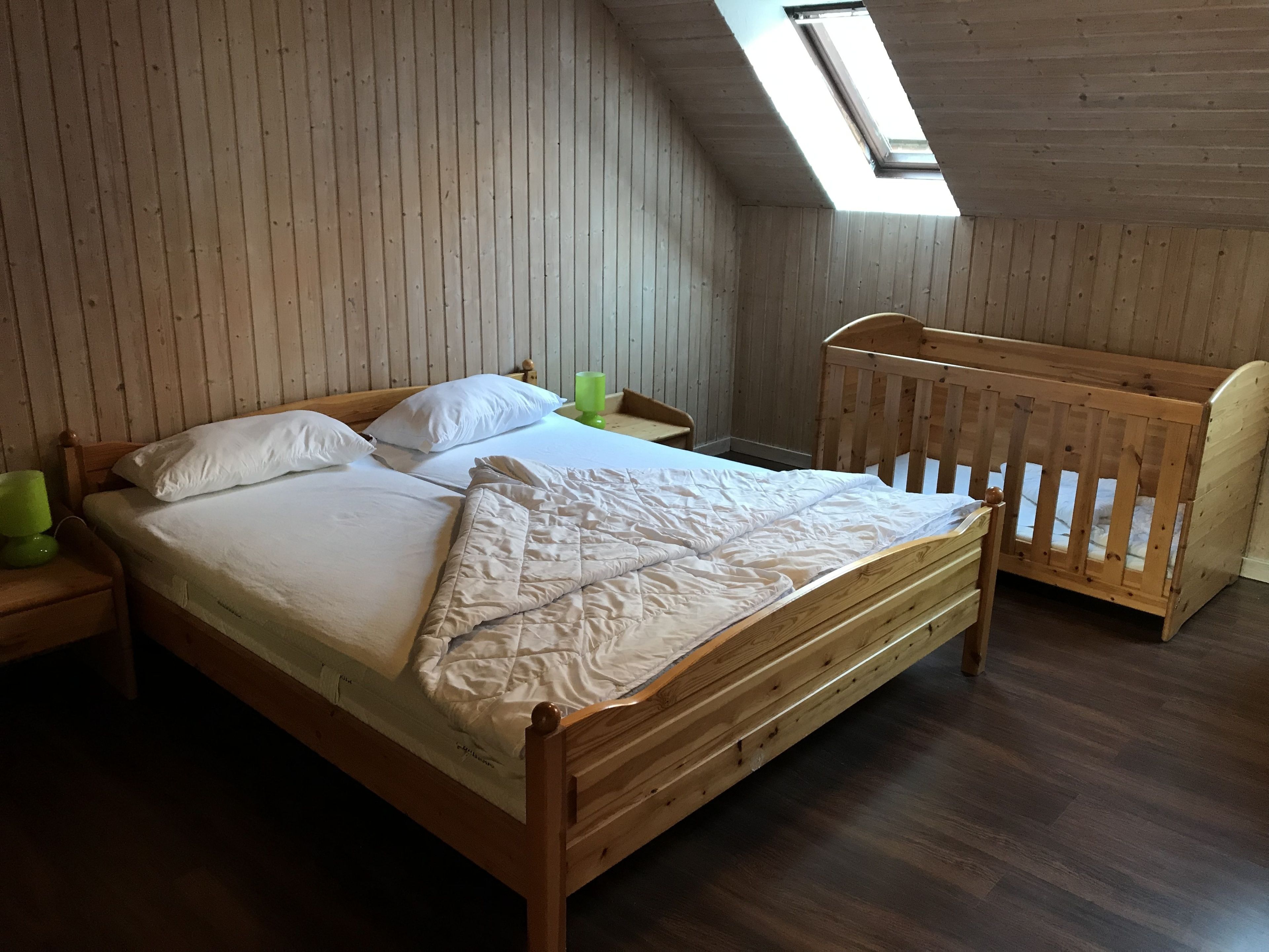 A wooden bed with white bedding in a room with wooden walls and a sloped ceiling.