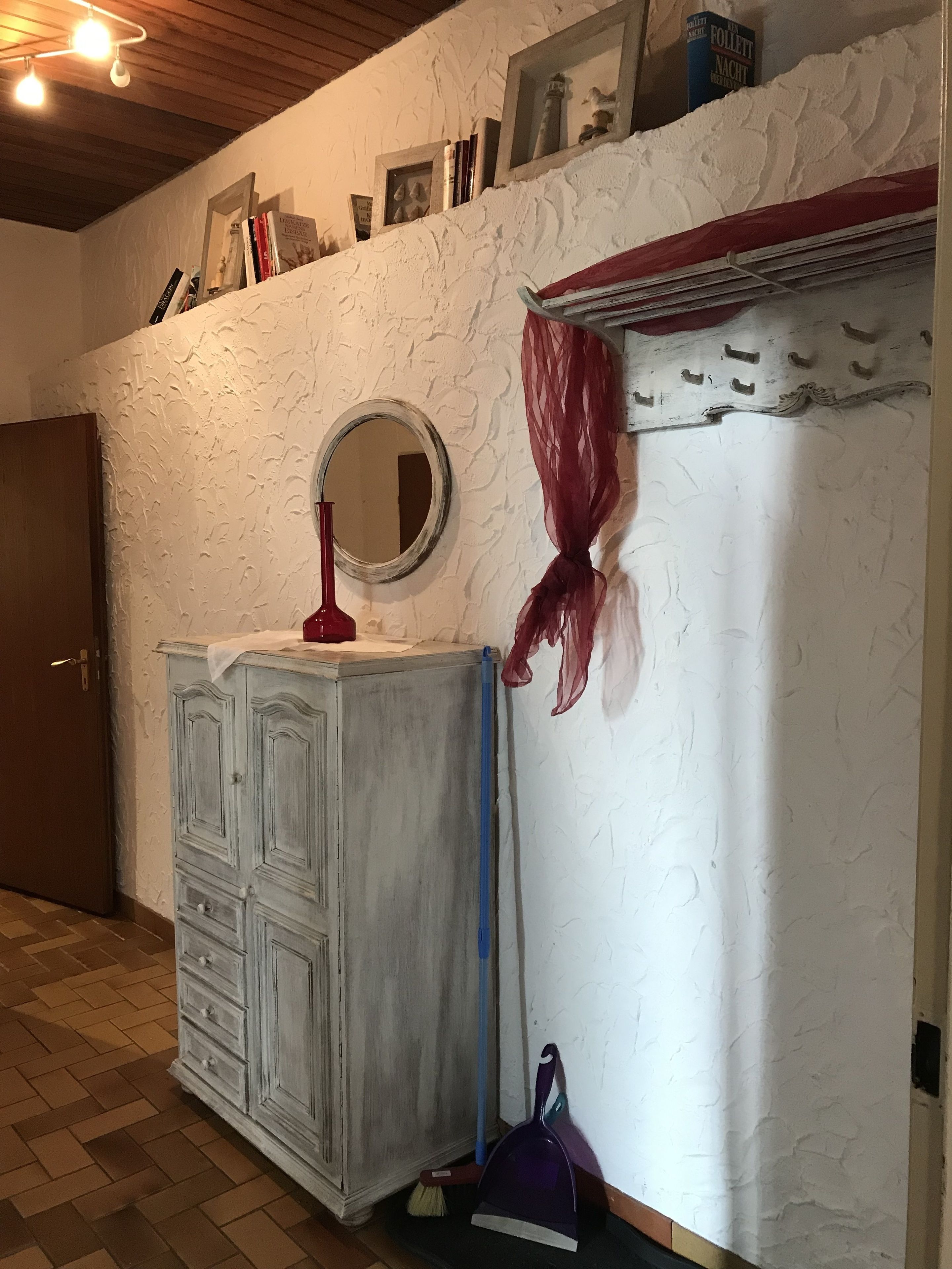 A room with a white textured wall, a wooden door, a white cabinet with drawers, a round mirror, and a red cloth draped over a window.