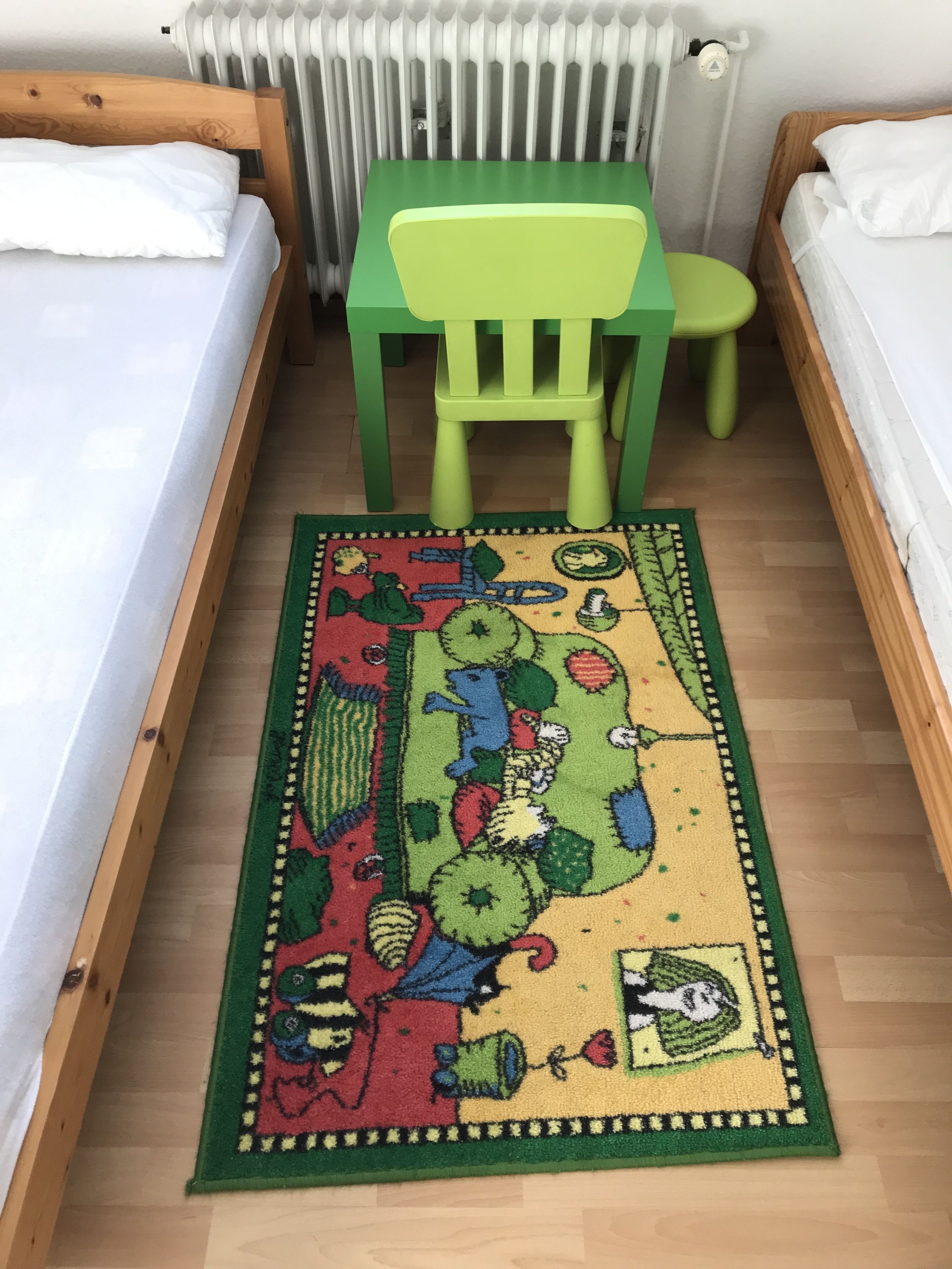 Ein Zimmer mit zwei Betten, einem grünen Sessel und einem farbenfrohen Teppich.