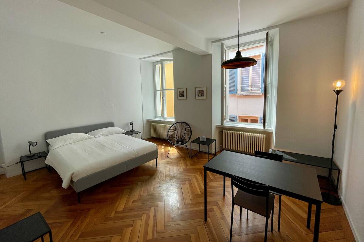 A bedroom with a bed, a table, a chair, a radiator, and a window.