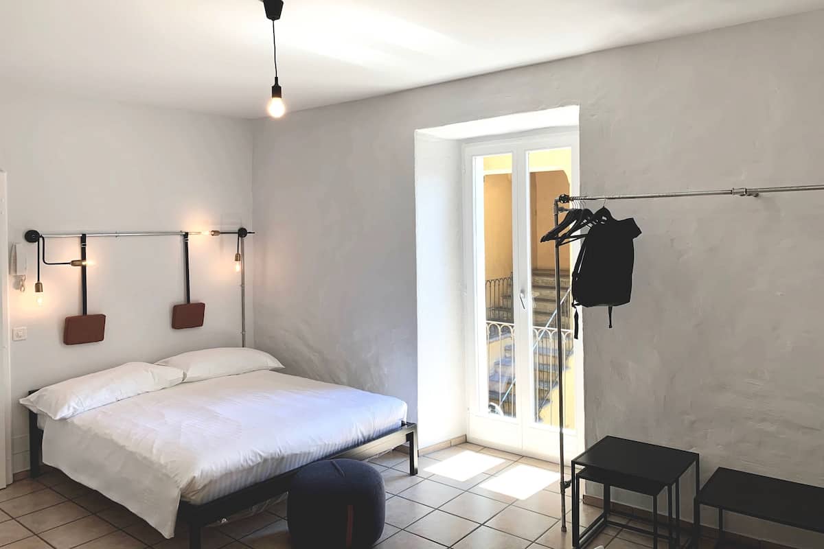A bedroom with a bed, a hanging light fixture, a coat rack, and a view of a staircase.