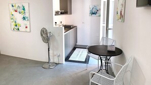 A modern kitchen with white cabinets, a built-in oven, and a microwave. There is a dining area with a round table and two white chairs.