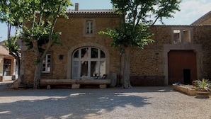 Un edificio de piedra con un amplio ventanal arqueado, un banco y un patio de grava.
