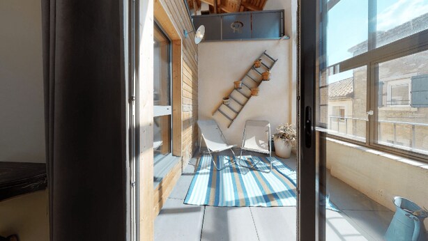 Un balcón con un tapete azul y blanco a rayas, una silla blanca y una escalera de madera apoyada en la pared.