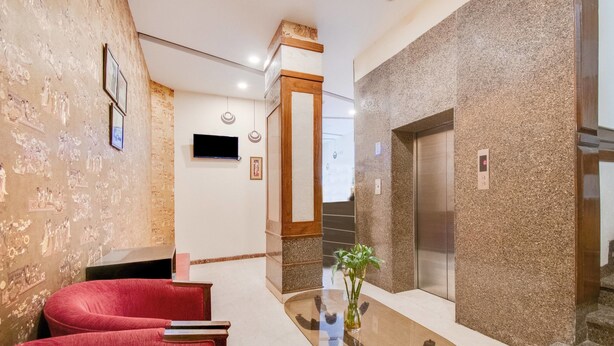 A lobby with a reception desk, a red sofa, a glass table with a vase, and an elevator. - Itsy Hotels Auzone & Spa (Chandigarh)